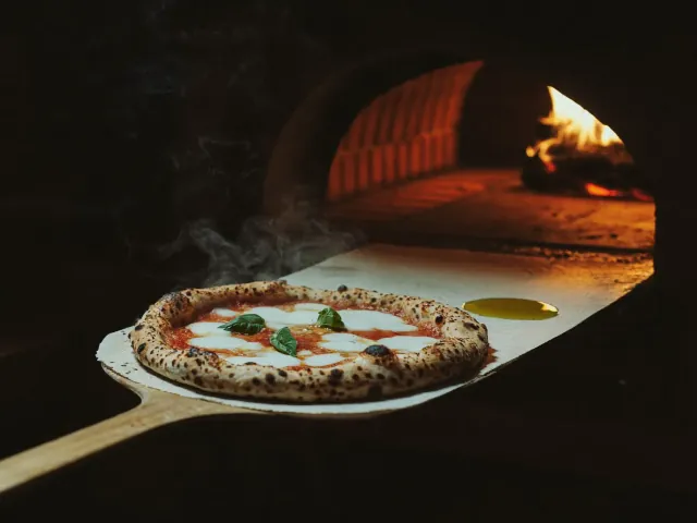 Zrzut ekranu strony Forno Rosso — pizza wyjmowana z rozgrzanego pieca opalanego drewnem